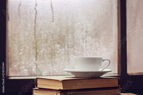 Cup of autumn tea (coffee, chocolate) and yellow leaves on rainy window, copy space. Hot drink for autumn mood.
