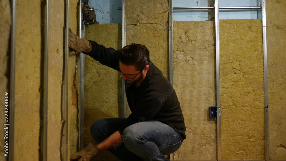 A home owner pushes in insulation into wall of unfinished basement A home owner pushes in insulation into wall of unfinished basement