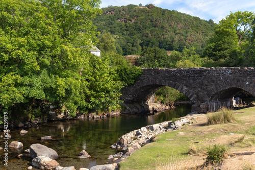 Old stone bridge over River Duddon in Ulpha in the Lake District National Park, UK. Scenic view of English countryside on a sunny day