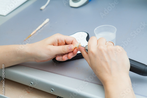 process of grinding the jaw during production. The dental technician processes artificial teeth with a micromotor. photo