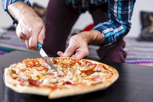 A man cuts the pizza on the table. Close-up.