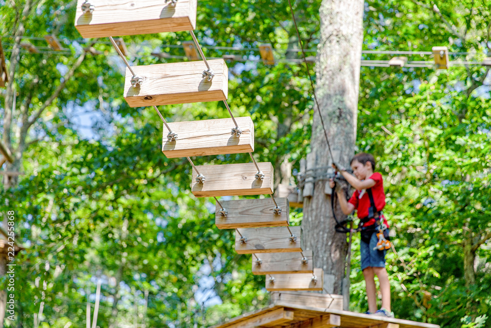 boy climbs in an aerial adventure park. child passes the rope obstacle. Blurred background. selective focus boy climbs in an aerial adventure park. child passes the rope obstacle. Blurred background. selective focus