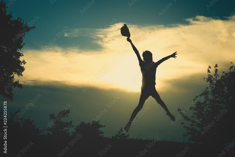 excited child joyfully jumps at sunrise. silhouette of person with hat outdoors. Copy space for your text