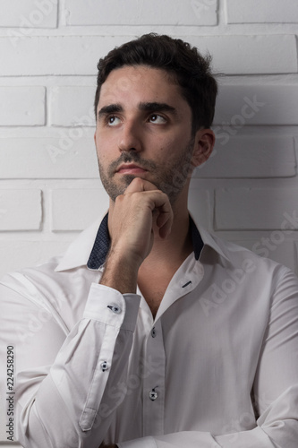 young white man wearing social outfit standing and posing in front of white brick wall photo