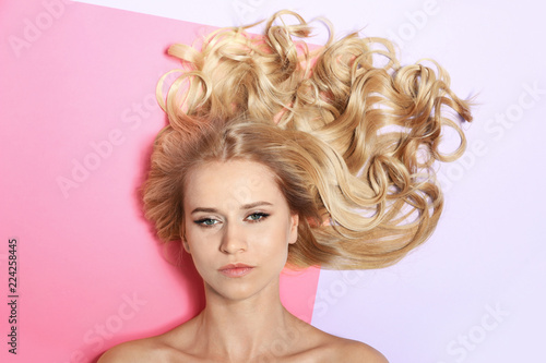 Beautiful woman with healthy long blonde hair on color background, top view