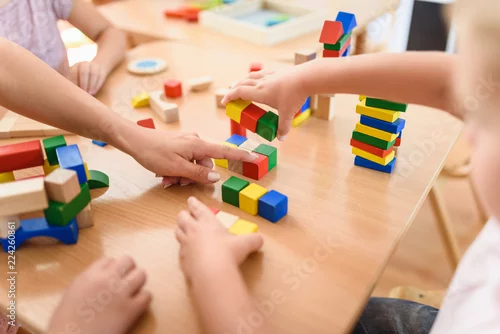Obraz Preschool teacher with children playing with colorful wooden didactic toys at kindergarten