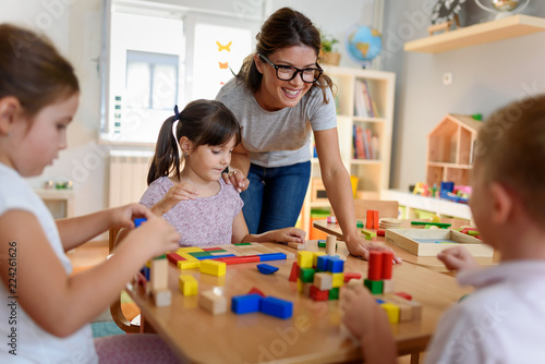 Canvas Print Preschool teacher with children playing with colorful wooden didactic toys at ki