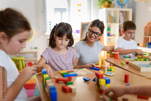 Obraz na plátně Preschool teacher with children playing with colorful wooden didactic toys at ki