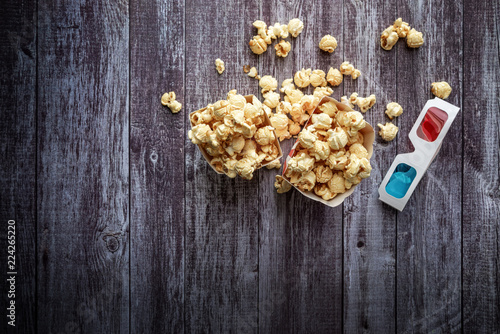 Cinema background, top view.  Popcorn and 3D glasses on wooden table. Movie accessories, cinematography concept, flat lay