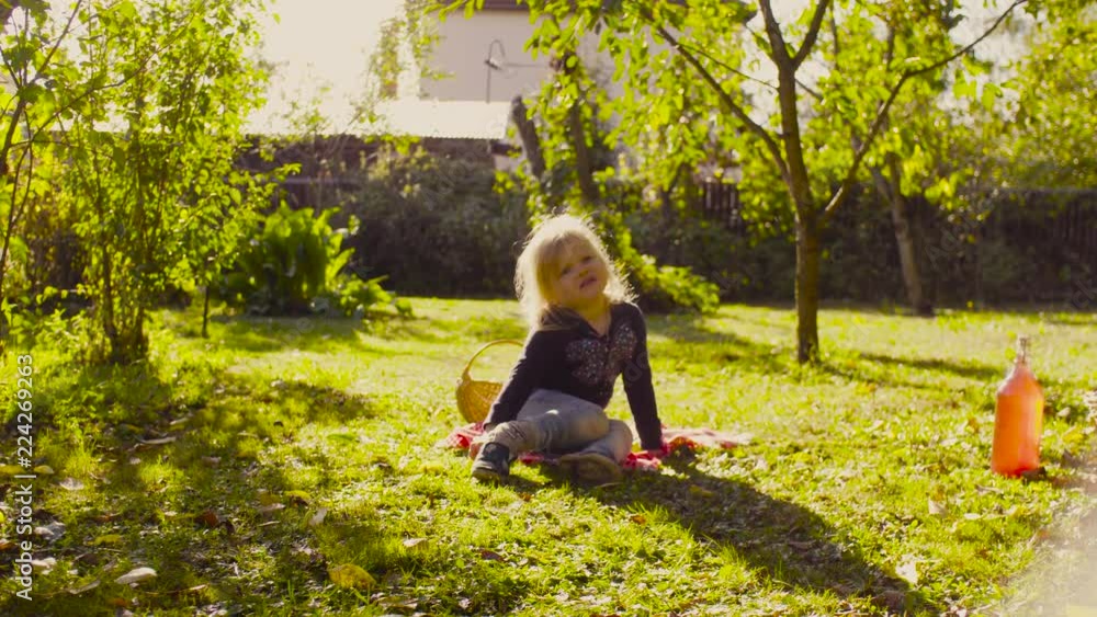 Crane shot. Funny little girl sitting on a grass in a garden and putting on her shoes on the wrong foot Crane shot. Funny little girl sitting on a grass in a garden and putting on her shoes on the wrong foot