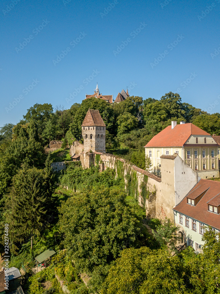 Aerial panorama of medieval Sighisoara in Romania with blue sky, red roofs, bastions, towers and city walls above the Mures river