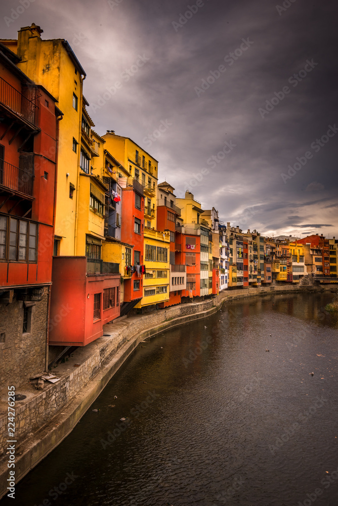 Colorful red, orange, yellow houses along the onyar river in medieval Girona, Catalonia north of Barcelona in Spain with stormy cloudy sky