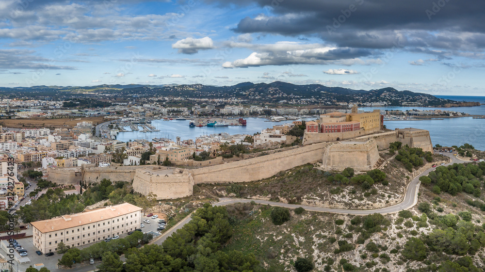 Aerial panorama of Ibiza town with fortifications, bastions, walls, churches, white houses against blue stormy cloudy sky