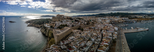 Aerial panorama of Ibiza town with fortifications, bastions, walls, churches, white houses against blue stormy cloudy sky