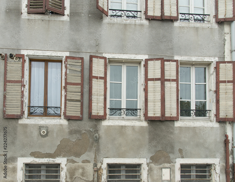 Obraz premium Wall of windows with faded and broken shutters on historic building in Europe