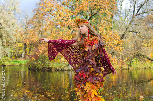 charming fairy of autumn in the yellowed forest stands on the shore of the forest lake with her arms outstretched