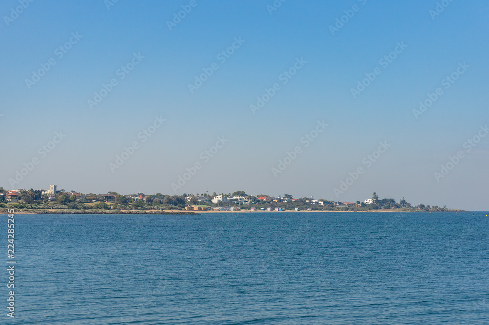 Ocean on sunny day with coastal town, suburb in the distance