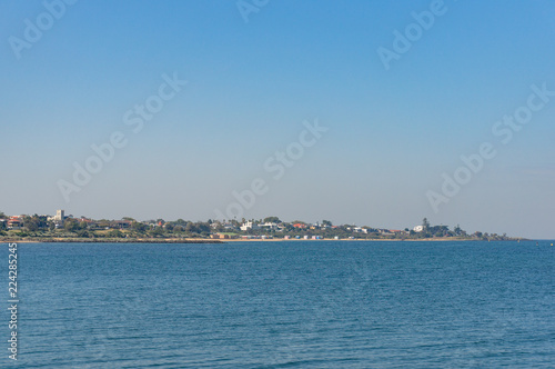 Ocean on sunny day with coastal town, suburb in the distance © Olga K