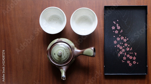 Flat lay of Japanese tea set consists of tea pot, tea cups and a black tray on wooden surface