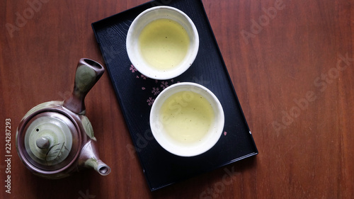 Flat lay of Japanese tea set consists of tea pot, tea cups and a black tray on wooden surface