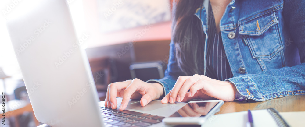 Women hand are using a computer laptop in the office.On the table are mobile phones. Notebook and pen.Web banner.