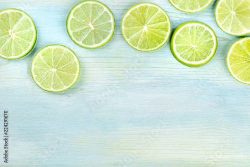 An overhead photo of many vibrant lime slices on a teal blue background