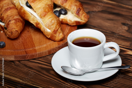 Cup of coffee with croissants, Camembert cheese, blueberries on a wooden background.
