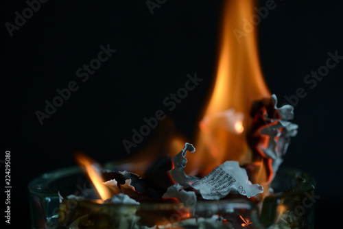 Fotografía A piece of paper burning in a glass ashtray close up