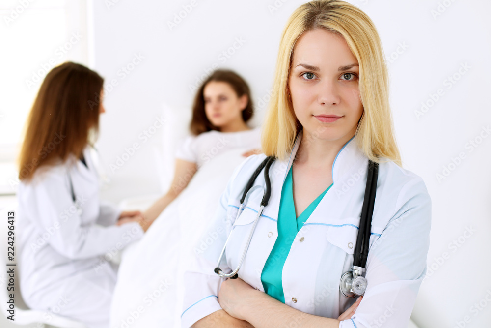 Doctor woman or nurse in a hospital office with her colleague and patient in the background. Healthcare and medicine concept Doctor woman or nurse in a hospital office with her colleague and patient in the background. Healthcare and medicine concept