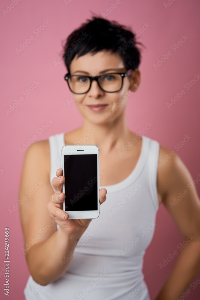 blurred beautiful woman with short hair shows the phone screen on a pink background