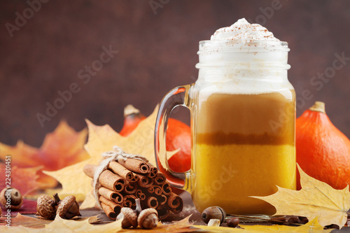Pumpkin spiced latte or coffee in glass jar decorated leaves on brown table. Autumn, fall or winter hot drink.