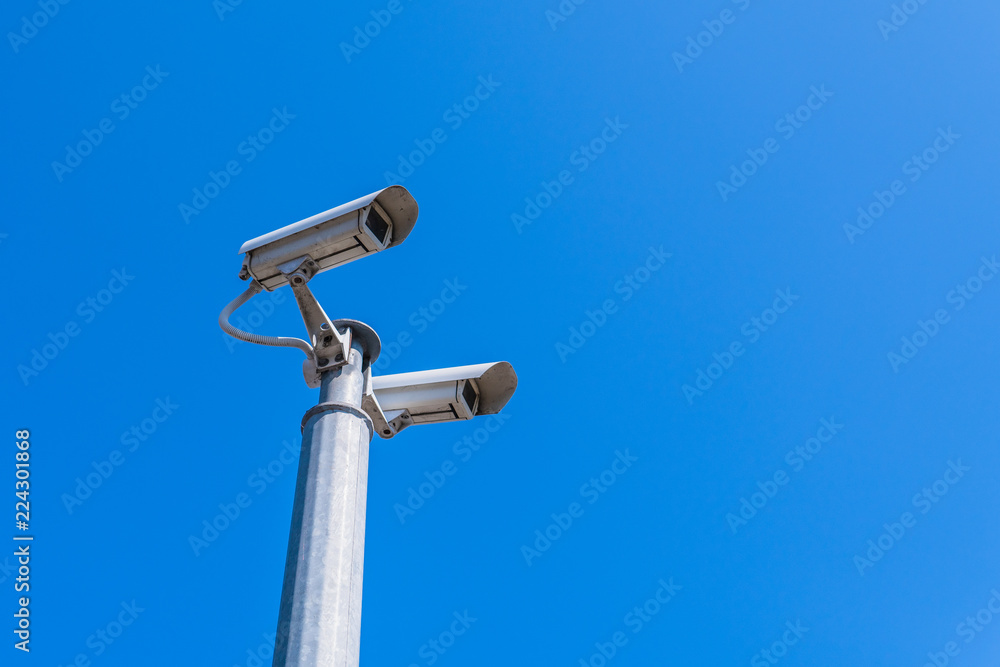 A modern CCTV security camera against blue sky background. A modern CCTV security camera against blue sky background.