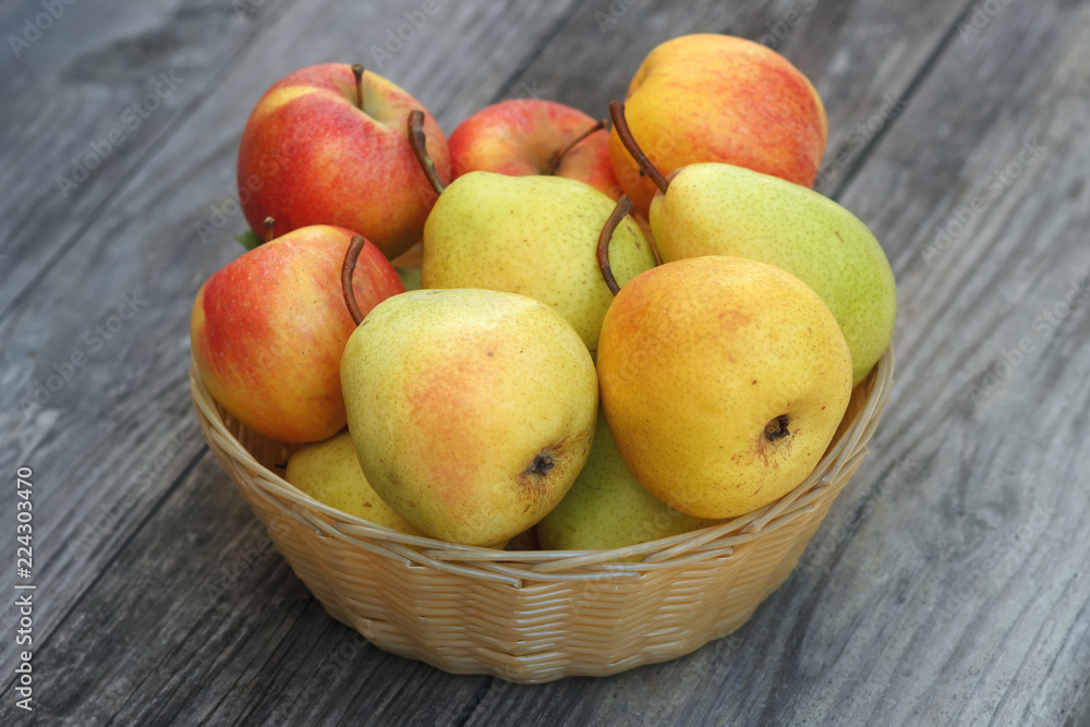 Fresh autumn apples and pears are collected in wicker basket on old wooden table 