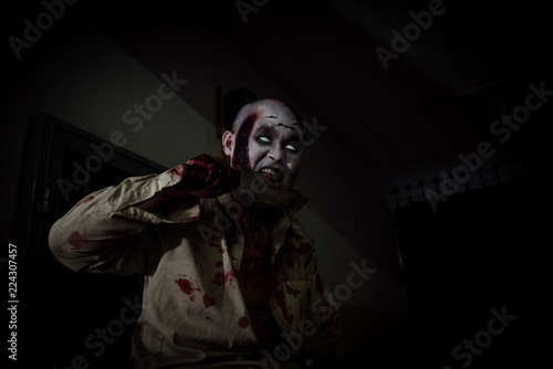 Male zombie holding and licking blood on knife in dark room