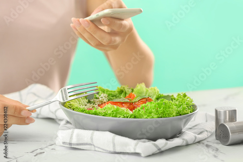 Woman taking photo of healthy salmon salad with mobile phone at table