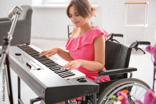 Canvas Print Beautiful young musician in wheelchair playing synthesizer at home