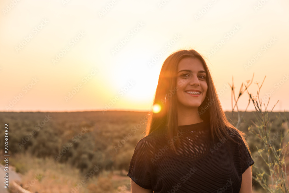 beautiful young girl walking on a road in the middle of the field at sunset