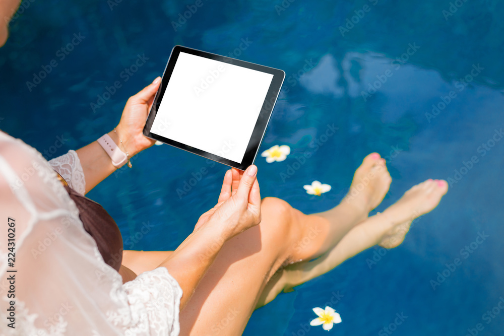 Woman sitting by the pool and using tablet computer. Horizontal screen orientation.