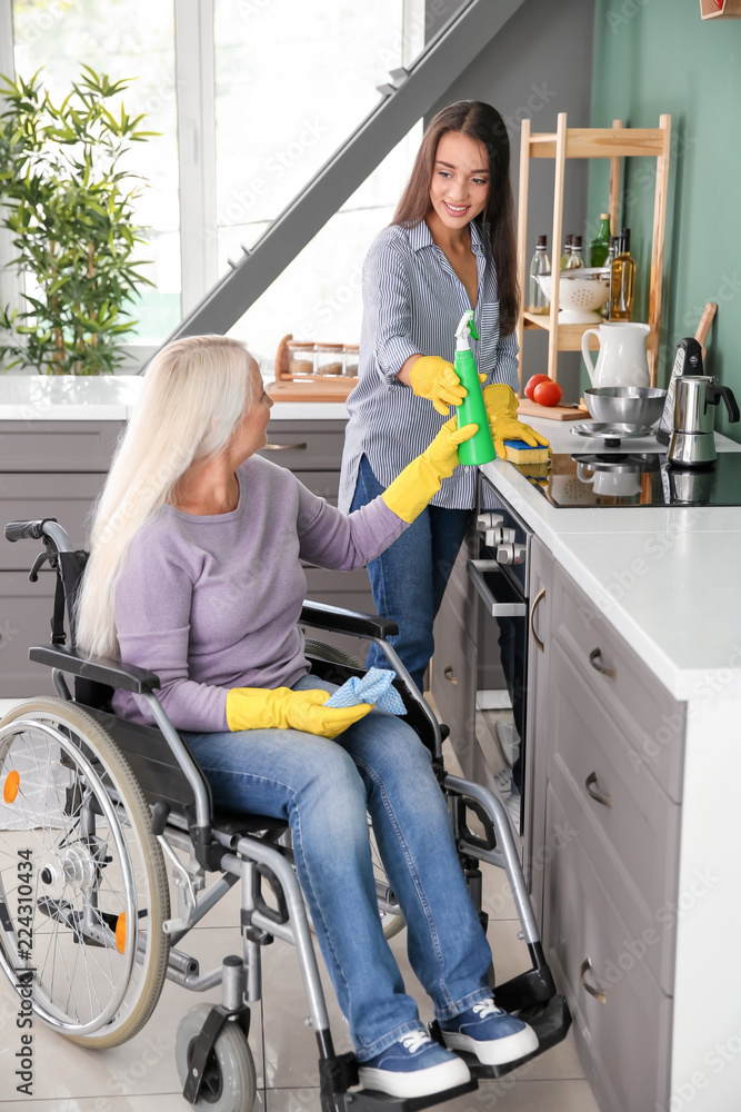 Mature woman in wheelchair cleaning kitchen together with daughter Stock  Photo | Adobe Stock