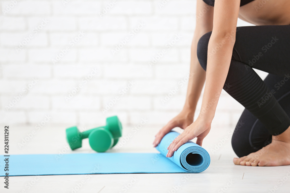 Young woman rolling yoga mat indoors
