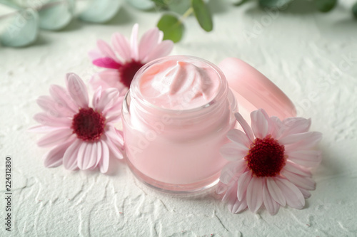 Jar with body cream and flowers on white table