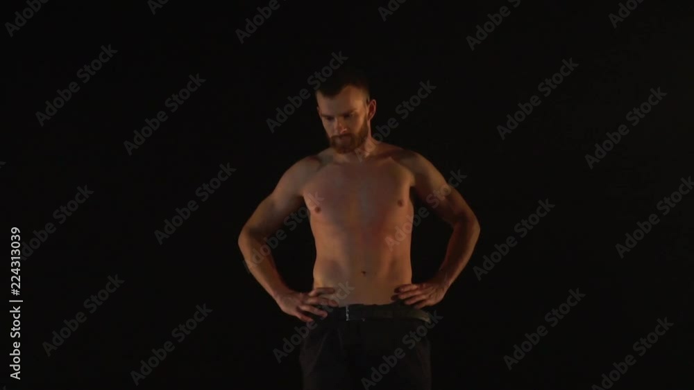 Muscular man stands topless against a black background Muscular man stands topless against a black background