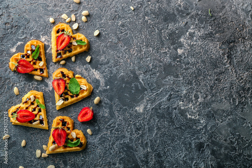 Heart shaped waffles with strawberries and nuts on grey background