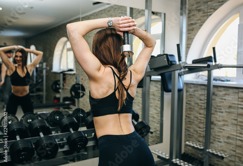 Beautiful girls with long hair is training in the gym with weights. Personal fitness trainer is at work doing exercises for good muscles. Sport motivation healthy lifestyle. Woman body workout.