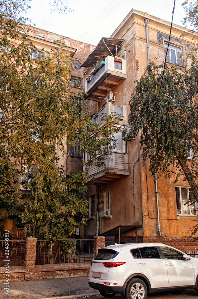 Fragment of an ancient house with balconies with a fence and trees with the parked car.