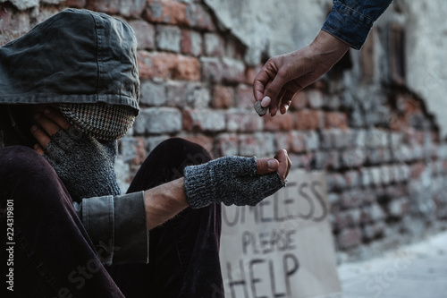 Картината върху платно Homeless man sitting on the street in the shadow of the building and begging for help and money