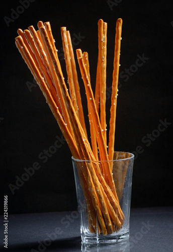 Pretzel sticks in small glass on black background photo