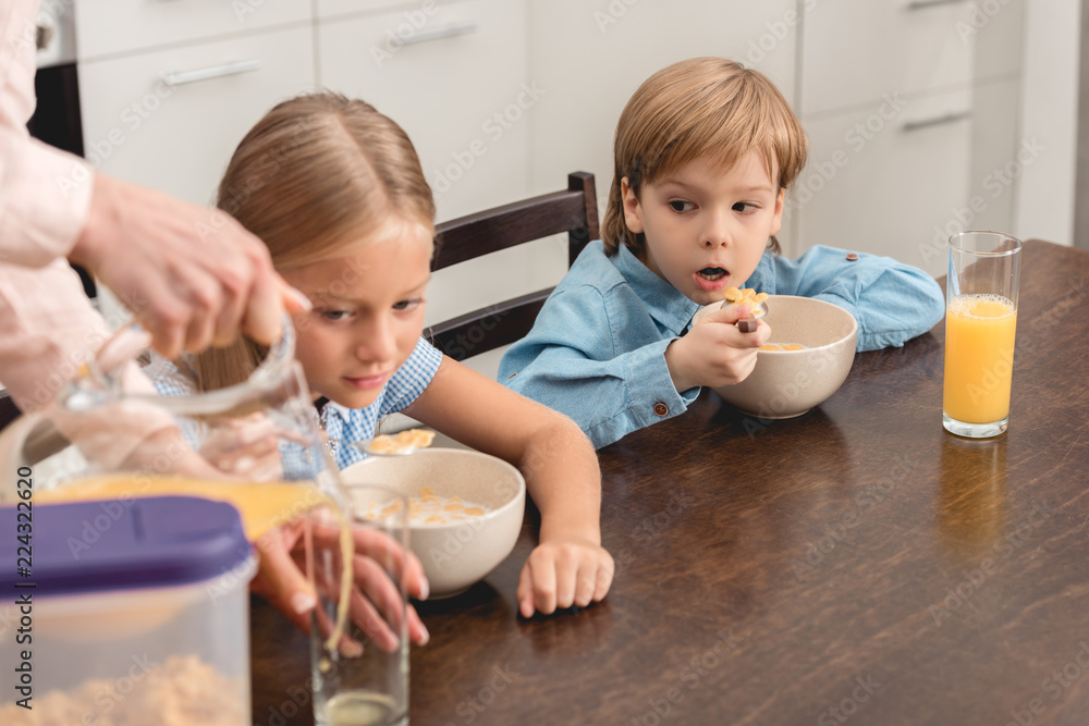 cropped shot of mother pouring orange juice for adorable little kids during breakfast cropped shot of mother pouring orange juice for adorable little kids during breakfast