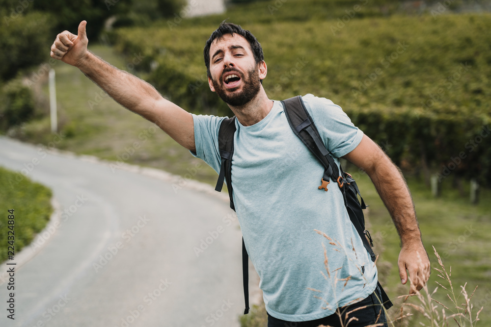 .Young and adventurous man hitchhiking on a side road of France surrounded by vineyards on a cloudy day. Travel photography. Lifestyle
