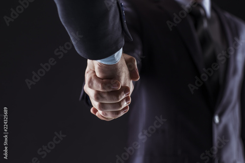 concept of a reliable partnership: a close-up of handshake of business partners on a black background.
